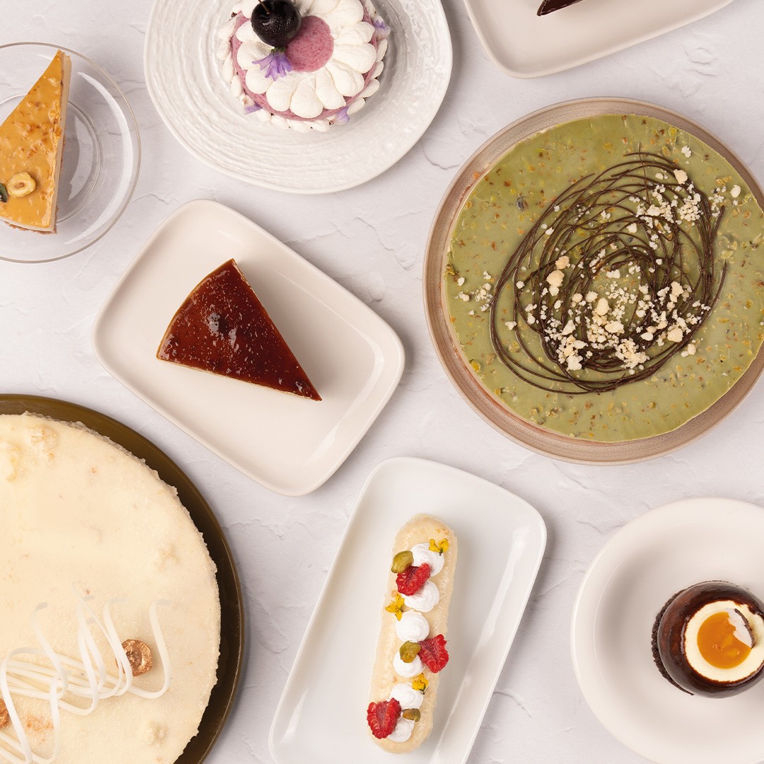 Vista superior de sobremesas variadas, incluindo cheesecake, pudim, tarte de pistácio, éclair e mousse de chocolate e...