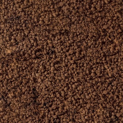 Plano aproximado de terra solta castanha ou borras de café com textura grossa e granulada a preencher o enquadramento.