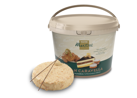 Balde grande de creme para barrar Master Martini Gran Caravella ao lado de uma fatia de bolo decorado.